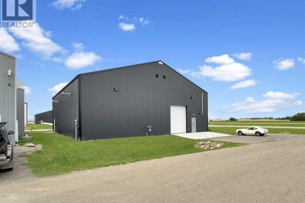 Side view of a dark grey metal hangar with a white garage door and a classic car. - 30, 1422 Township Rd 320a, Didsbury