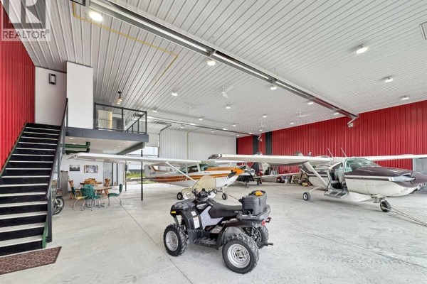 Interior of a hangar with aircraft, an ATV, stairs, and an office space. - 30, 1422 Township Rd 320a, Didsbury