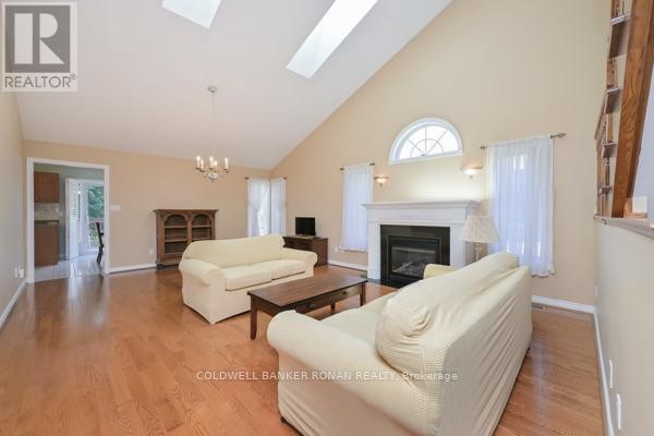 Living room with vaulted ceiling, skylights, fireplace, wood floors, and two cream-colored sofas. - 30 - 43 Briar Gate, New Tecumseth