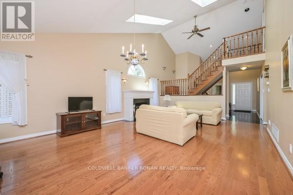 Spacious living room with fireplace, vaulted ceiling, skylights, wood floors, and a view of the staircase and entryway. - 30 - 43 Briar Gate, New Tecumseth