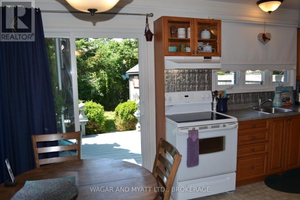 Kitchen with wooden cabinets, white stove, and sliding glass doors opening to a backyard deck. - 30 - 60 Winchester Drive, Greater Napanee