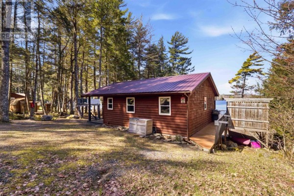 View of the red cabin from the side, showing the wooden deck and surrounding trees with a lake in the distance. - 30 11-15 Road, Hibernia