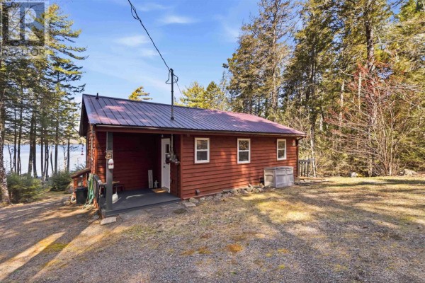 Front view of the red cabin from a slight angle, showing the entrance, porch, and surrounding natural landscape. - 30 11-15 Road, Hibernia