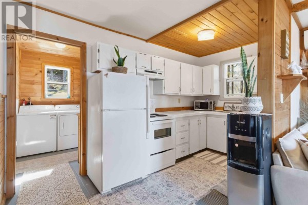 White kitchen with wooden ceiling and trim, featuring a refrigerator, stove, microwave, and doorway to a laundry area. - 30 11-15 Road, Hibernia