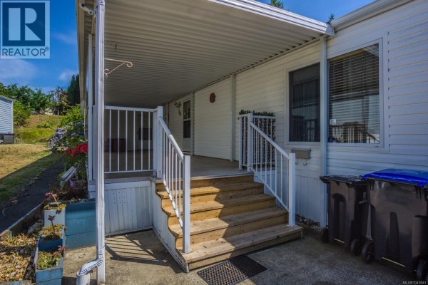 Covered front porch with wood stairs, white railings, and trash bins next to the entrance. - 30 4714 Muir Rd, Courtenay
