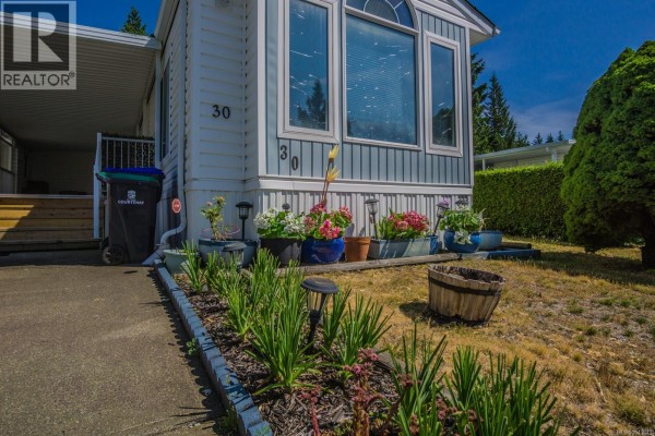 Close-up of the front of the mobile home with flower planters along the driveway. - 30 4714 Muir Rd, Courtenay