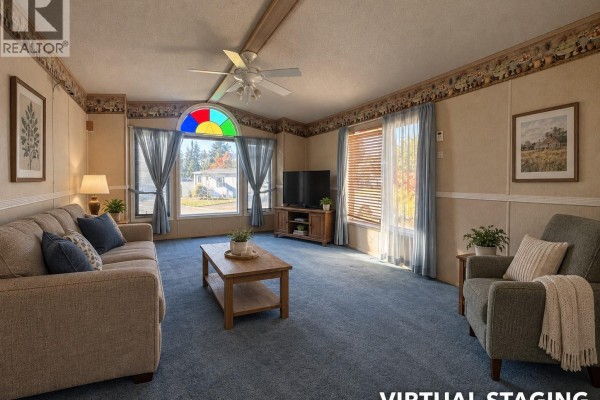 Living room with blue carpet, beige paneled walls, and large windows overlooking the street. - 30 4714 Muir Rd, Courtenay