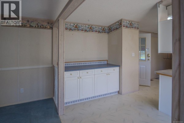 Living room with blue carpet, beige paneled walls, and a stained-glass arched window above the main window. - 30 4714 Muir Rd, Courtenay