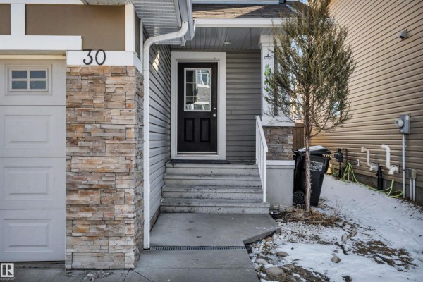 Interior view of a duplex entryway with white doors, a dark wooden vase with greenery, and a small shelf. - #30 655 Tamarack Rd Nw, Edmonton