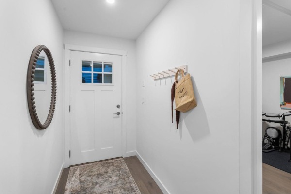 Interior entryway with white walls, a wooden floor, a round mirror, and a coat rack. - 30 9122 King Street, Langley