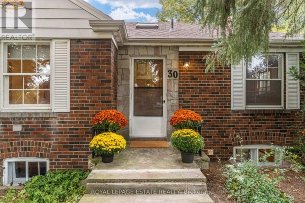Close-up of the front entrance of a red brick house with a stone surround and fall mums. - 30 Barbara Crescent, Toronto