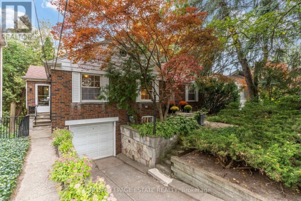 Side view of the brick house with a driveway leading to a white garage door and landscaping. - 30 Barbara Crescent, Toronto