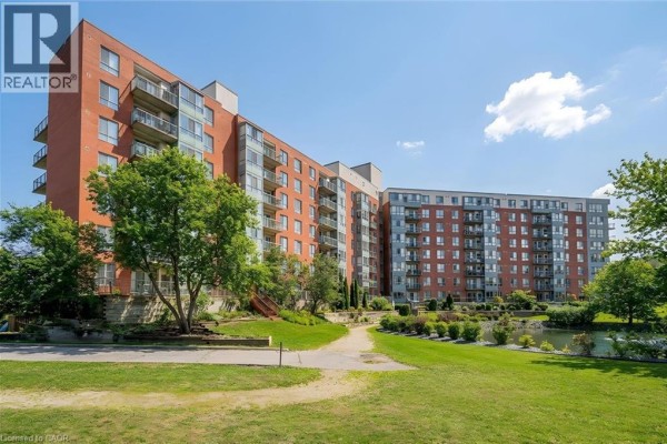 Side view of the brick apartment building with mature trees and a pond in the foreground. - 30 Blue Springs Drive Unit# 307, Waterloo