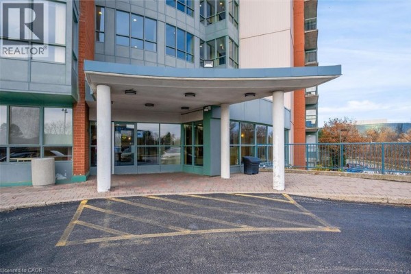 Covered entrance to the apartment building with glass doors, brick columns, and paved walkway. - 30 Blue Springs Drive Unit# 307, Waterloo