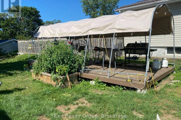 Deck in the backyard covered by a large tarp, with a grill and propane tanks visible. - 30 Bocage Street, Quinte West