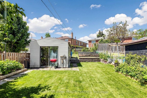 Backyard view of a brick house with a covered porch, green lawn, and wooden fence. - 30 Clubhouse Court, Toronto