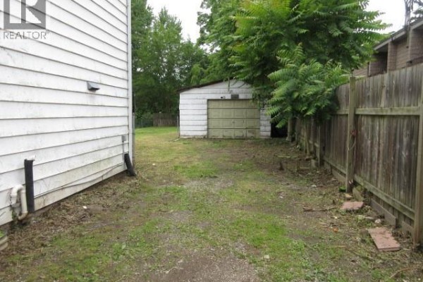 Backyard view showing a gravel driveway, a detached garage, and a wooden fence. - 30 Delaware Avenue, Chatham