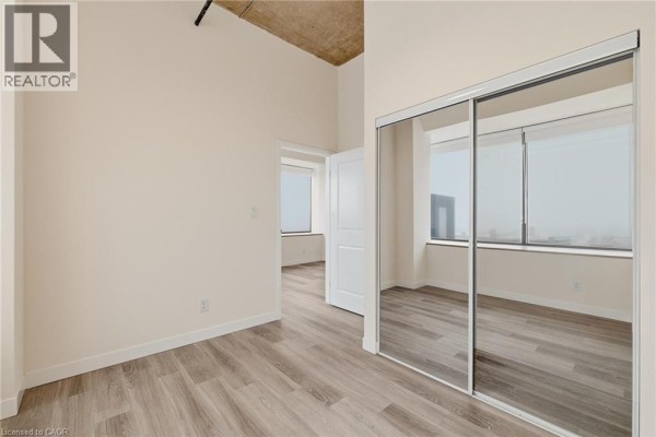 Bedroom area with large window, light wood flooring, and adjacent bathroom entry. - 30 Duke Street W Unit# 315, Kitchener