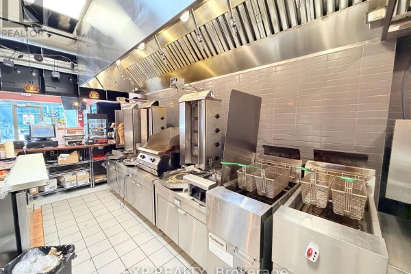 Commercial kitchen with stainless steel appliances including fryers, grills, and shawarma rotisseries. - 30 Eglinton Avenue W, Mississauga