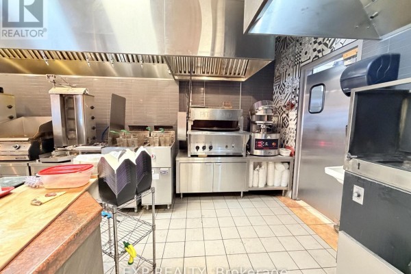 Commercial kitchen featuring a pizza oven, shawarma rotisserie, and stainless steel hoods and counters. - 30 Eglinton Avenue W, Mississauga
