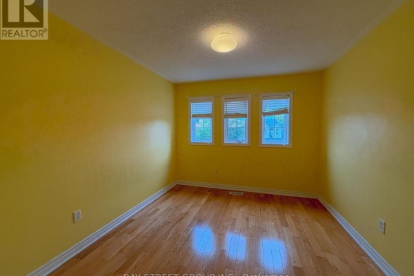 Bedroom with bright yellow walls, hardwood floors, and three windows. - 30 Emery Hill Boulevard, Markham