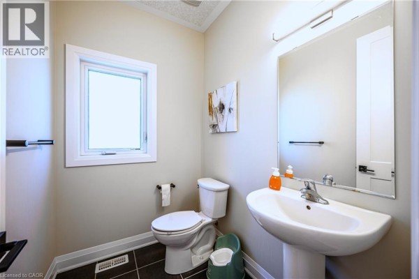 Small bathroom with a white toilet, pedestal sink, mirror, and tan walls. - 30 Falconridge Drive Unit# Upper, Kitchener