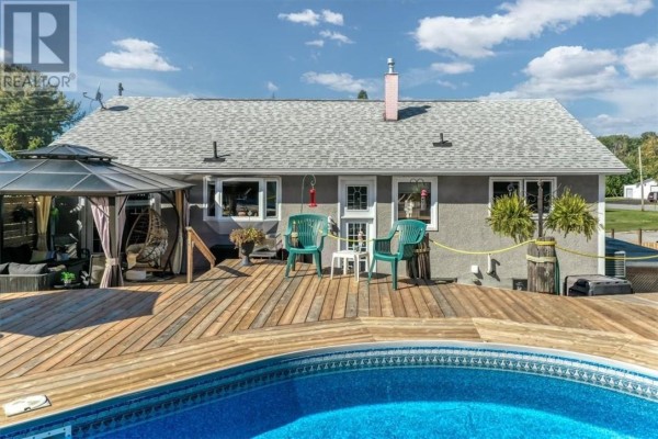 Backyard view of the house with a large wooden deck and a blue pool. - 30 Fir St, Onaping