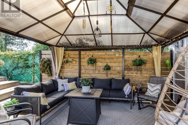 Covered outdoor living space with dark grey sectional sofa, fire pit table, and hanging chair. - 30 Fir St, Onaping