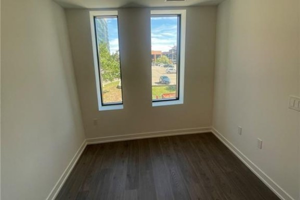 Interior view of a room with dark wood floors and two tall windows overlooking an urban street. - 30 Francis Street S Unit# 207, Kitchener