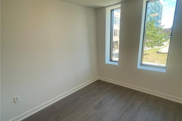Interior view of a room with dark wood floors and two tall windows showing urban scenery. - 30 Francis Street S Unit# 207, Kitchener