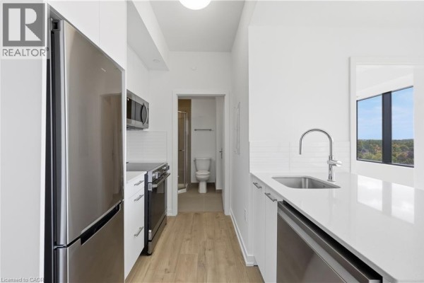 Galley kitchen with stainless steel appliances and doorway to bathroom. - 30 Francis Street S Unit# 602, Kitchener