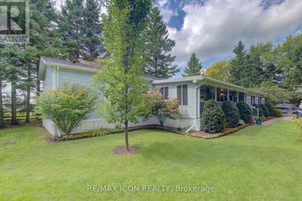 Side view of a light blue mobile home with green grass and mature trees in the yard. - 30 Grand Vista Crescent, Wellington North