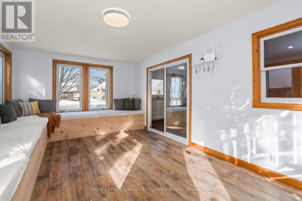 Sunroom with a sliding glass door to the kitchen, large windows, wooden bench seating, and light wood floors. - 30 Kitchen Road S, Huntsville