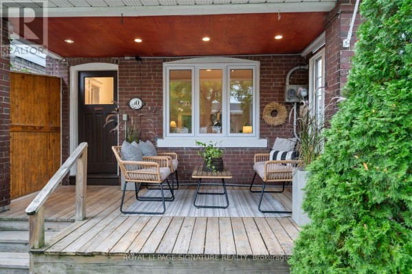 Close-up of the covered wooden porch with rattan chairs, a coffee table, and decorative planters. - 30 Lawlor Avenue, Toronto