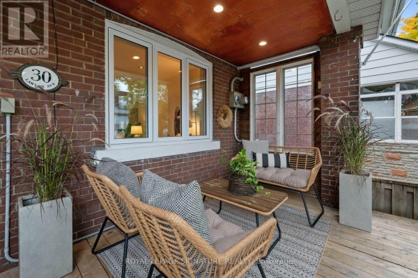 Another view of the porch seating area, showing a loveseat, coffee table, and large potted plants. - 30 Lawlor Avenue, Toronto