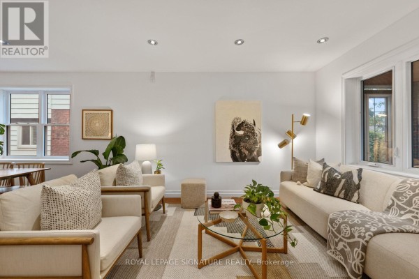 Living room with white sofas, a glass coffee table, wood flooring, and artwork on the walls. - 30 Lawlor Avenue, Toronto