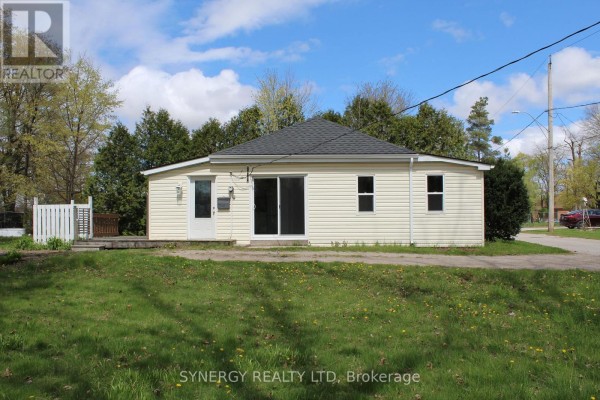 Side exterior view of a beige vinyl-sided house with a gravel driveway and green trees. - 30 Mill Lane, Strathroy Caradoc