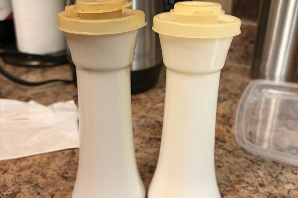 Two vintage white milk glass salt and pepper shakers with yellow lids on a counter. - 30 Monroe Street, St John S