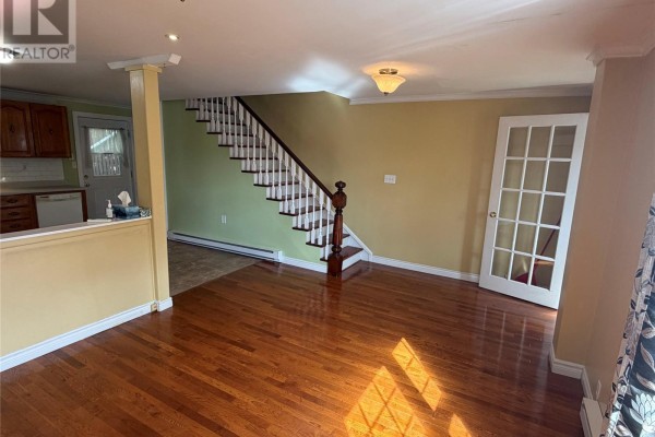 Living room with yellow walls, hardwood floors, a staircase, and a glass-paneled door. - 30 Monroe Street, St John S