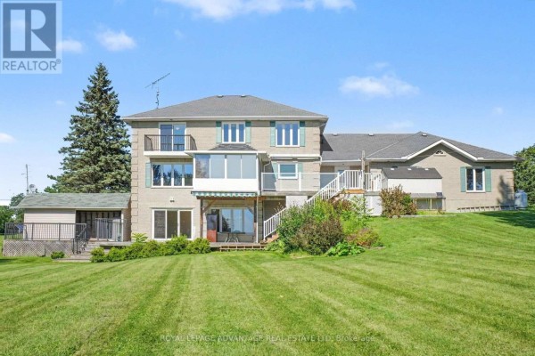 Rear exterior view of a multi-level house with a walk-out basement and a green lawn sloping downwards. - 30 R14 Road, Rideau Lakes