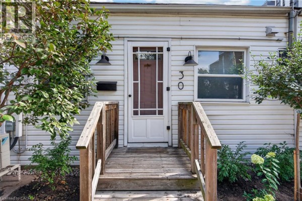 Close-up of the front door and wooden porch steps of a townhouse with light siding. - 30 Ray Street N, Hamilton