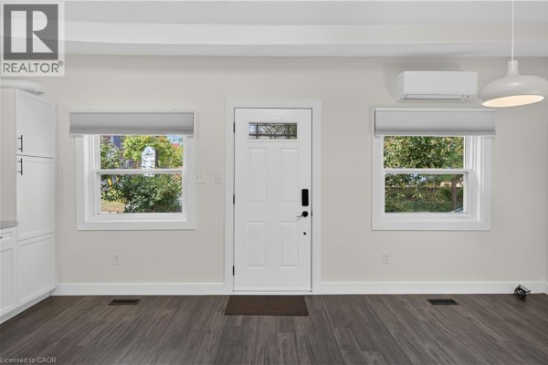 Interior view of a townhouse entrance with white door, two windows, and grey wood floors. - 30 Ray Street N, Hamilton