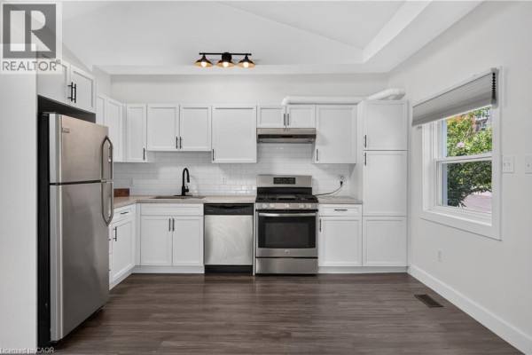 Modern white kitchen with stainless steel appliances, grey subway tile backsplash, and dark wood floors. - 30 Ray Street N, Hamilton