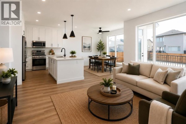 Open-concept kitchen with white cabinets, island, stainless steel appliances, and large windows. - 30 Rivergrove Run W, Lethbridge