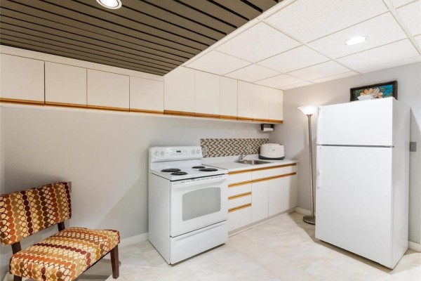 Small basement kitchen with white appliances, white cabinets, mosaic backsplash, and a patterned chair. - 30 Riverview Crescent, Lorette