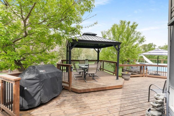 Wooden deck with a gazebo, dining set, grill, and view of the backyard pool. - 30 Riverview Crescent, Lorette
