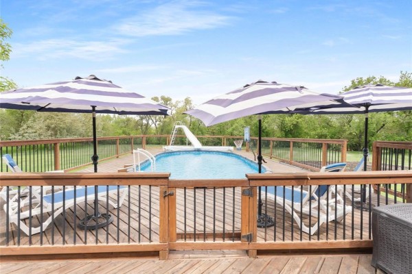 Backyard deck with lounge chairs, striped umbrellas, and an oval swimming pool with a slide. - 30 Riverview Crescent, Lorette