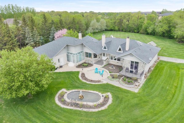 Aerial view of a large stone and stucco home with a sprawling green lawn and mature trees. - 30 Riverview Crescent, Lorette
