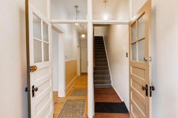 Interior view of a hallway with wood floors, leading to a carpeted staircase and open doors. - 30 Robert Street, Toronto