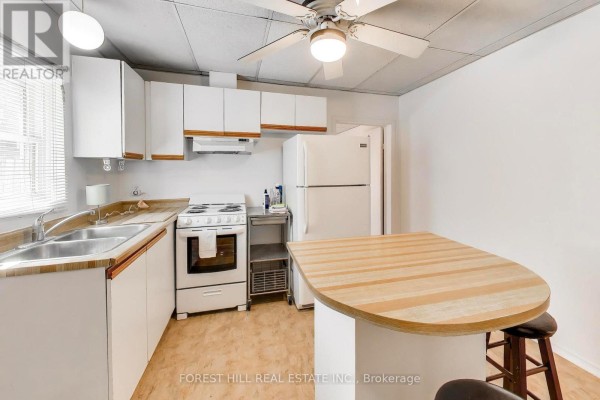 Kitchen with breakfast bar, white cabinets, stove, fridge, and ceiling fan - 30 Robert Street Toronto